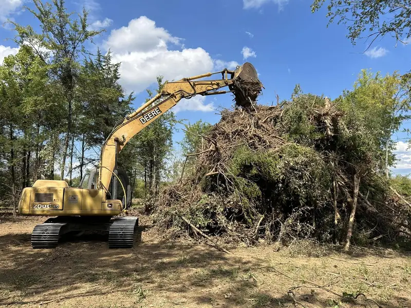 Excavator piling cleared brush and trees on a property