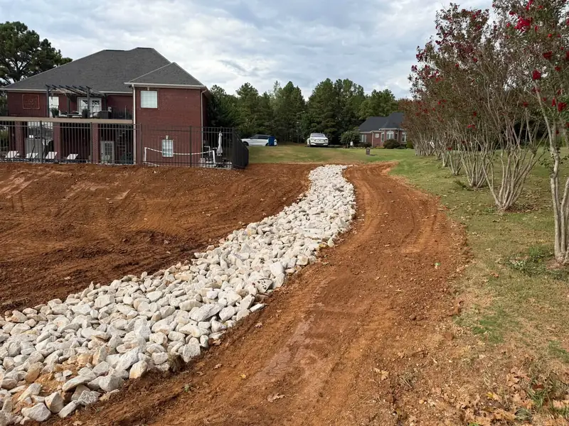 Drainage swale lined with rip rap behind a brick house