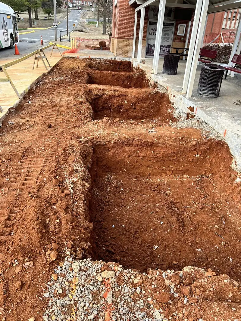 Footing trenches excavated in red clay next to a building